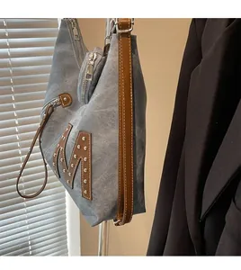 Detail of blue denim tote bag with brown leather M patch, silver rivets and long strap