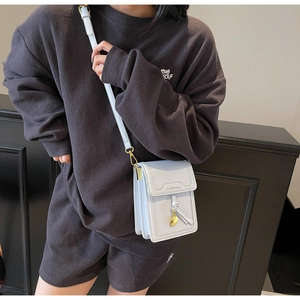 Close-up of light blue leather phone bag featuring gold brand logo and metal ring charm