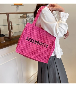 Detail of fuchsia woven tote bag featuring black Serendipity text and wide handles