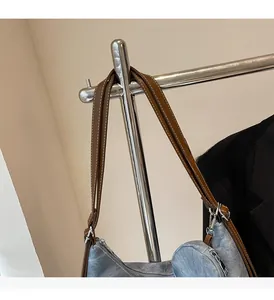 Detail of light blue denim tote with brown leather handles and silver zipper hardware