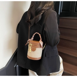 Detail of woven cylinder bucket bag with silk scarf handle and gold metal zippers