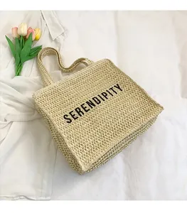 Detail of beige woven straw tote bag with black Serendipity text and twin handles