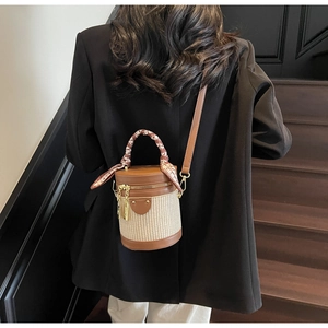 Detail of elegant cylinder bucket bag with woven body and silk scarf handle accent