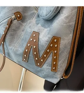 Detail of blue denim tote bag with leather M letter and silver stud accents