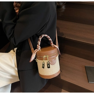 Detail of cylinder bucket bag featuring woven straw texture and silk scarf handle wrap