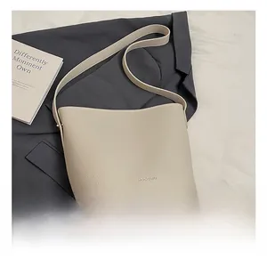 Detail of a creamy white lychee grain bucket bag with brand embossing and leather strap