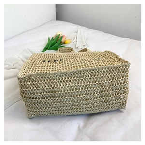 Detailed close-up of large straw woven bag with black embroidered text on white bedding