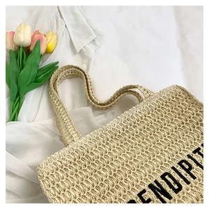 Detail of woven straw tote bag featuring black Serendipity embroidery and fine texture