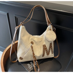 Detail of canvas tote bag showing decorative metal stud M logo and mini coin purse