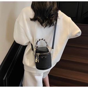 Detail of black cylinder bucket bag with silk scarf handle and gold metal lock charm