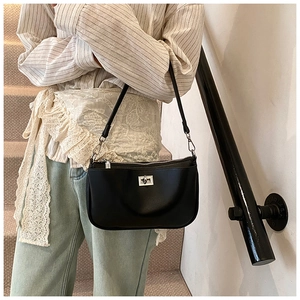 Detail of a black underarm bag featuring a silver twist lock and zipper on a model