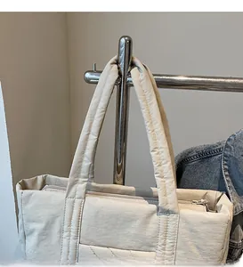 Detail view of a beige quilted puffer tote bag with soft straps hanging on a metal rack