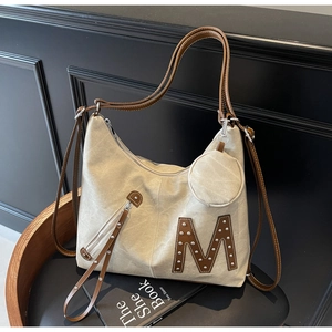 Canvas tote bag detail showing M patch, metal rivets and round coin purse attachment