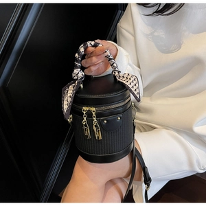 Detail of black cylinder bag with silk scarf handle and golden chain zip pullers