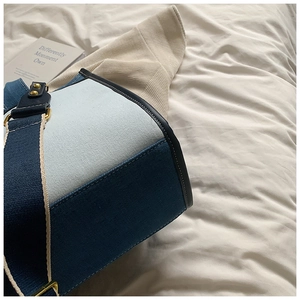 Détail d'un sac cabas en denim contrasté avec boucle dorée sur tissu blanc doux