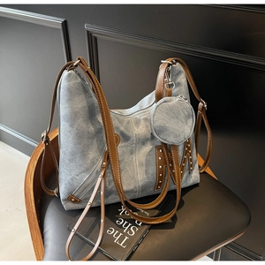 Detail of blue denim tote bag with brown leather straps and metal rivet M-patch