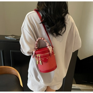 Detailed view of red woven bucket bag featuring silk scarf handle and gold hardware