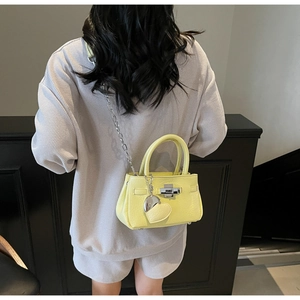 Detail of light yellow leather bucket bag with silver heart charm and chain strap