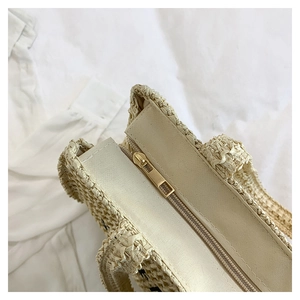 Detail of the golden metal zipper closure and woven texture on a beige straw beach bag