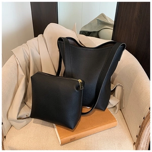 Detail of black litchi leather bucket bag set with golden hardware on a soft chair