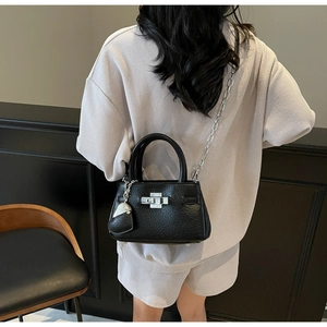 Detail of black lychee-textured mini bucket bag with silver lock and heart charm