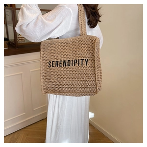 Detail of handwoven straw tote bag with Serendipity lettering and wide shoulder straps