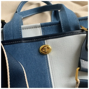 Vue détaillée du fermoir rotatif doré et des coutures sur le sac cabas en denim