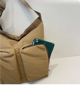 Detail of khaki nylon tote bag showing a tablet inside the large front zipper pockets