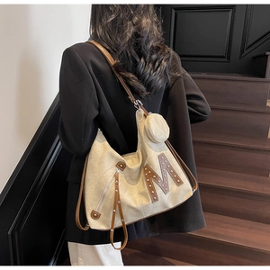 Detail of canvas hobo bag with studded M logo and brown leather strap on model