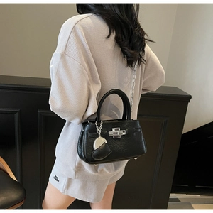 Detail of black pebbled leather bucket bag with silver chain strap and heart charm