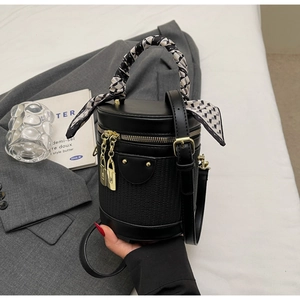 Close-up of black cylinder bag with woven texture, silk scarf handle, and gold hardware