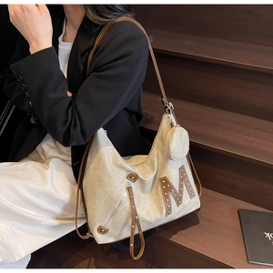 Detail of canvas tote bag with brown leather M logo, silver studs, and round coin purse