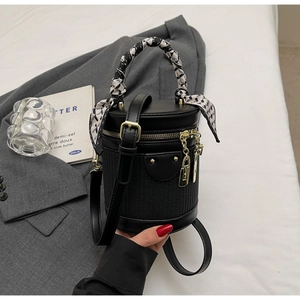Detail of black cylindrical bucket bag with woven texture, gold zipper and silk scarf