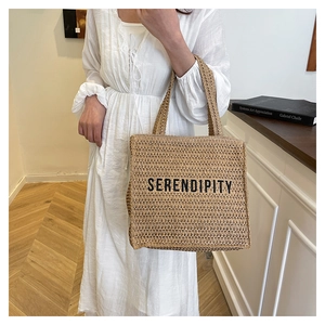 Detail of handwoven straw tote bag with black SERENDIPITY text print and sturdy handles