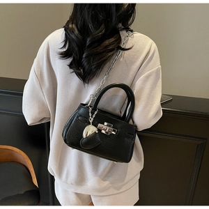 Detail of black leather bucket bag with silver chain strap and heart charm accessory