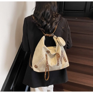 Detail of beige canvas tote with brown leather trim, silver studs and letter M patch