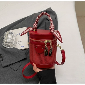 Detail of red cylindrical bag with woven texture, gold locks, and silk scarf handle