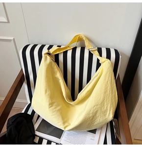 Detail der hellgelben Nylon-Tasche mit Faltenstruktur auf einem gestreiften Stuhl