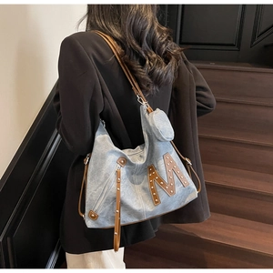 Detail of denim blue hobo bag featuring rivet M logo and mini round coin purse attachment