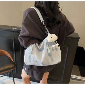 Détail d'un sac à bandoulière bleu clair avec breloque nuage en peluche et zip métallique