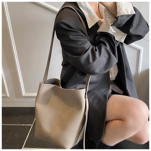 Close-up of beige lychee-patterned leather bucket bag worn by model in business attire
