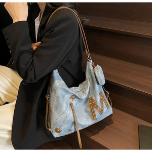 Blue denim tote bag with brown M patch and mini coin purse shown on a model