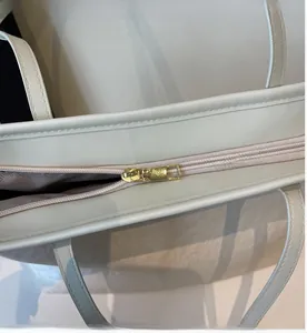 Close-up of smooth gold zipper and grain leather texture on white tote bag