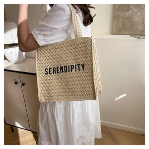 Detail view of woven straw tote bag featuring the Serendipity print text and fiber texture