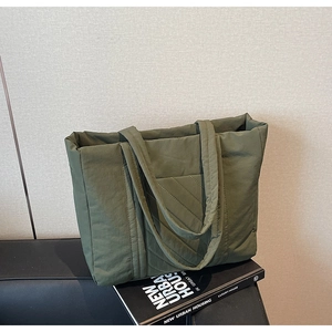 Detailed view of the olive green quilted nylon tote bag placed on a black book