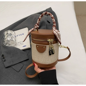 Detail view of cylinder bucket bag with woven texture and decorative silk handle wrap