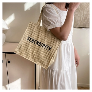 Detail of woven straw tote bag with black SERENDIPITY text and large capacity