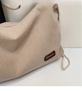 Close-up of beige knitted tote bag featuring vertical texture and brown leather brand patch