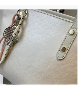 Detail of white tote bag with crinkled texture, tennis racket charm and gold rivets