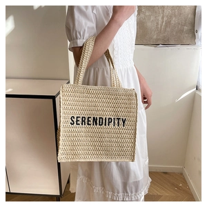 Detail of handwoven straw tote bag with black SERENDIPITY embroidery on cream texture